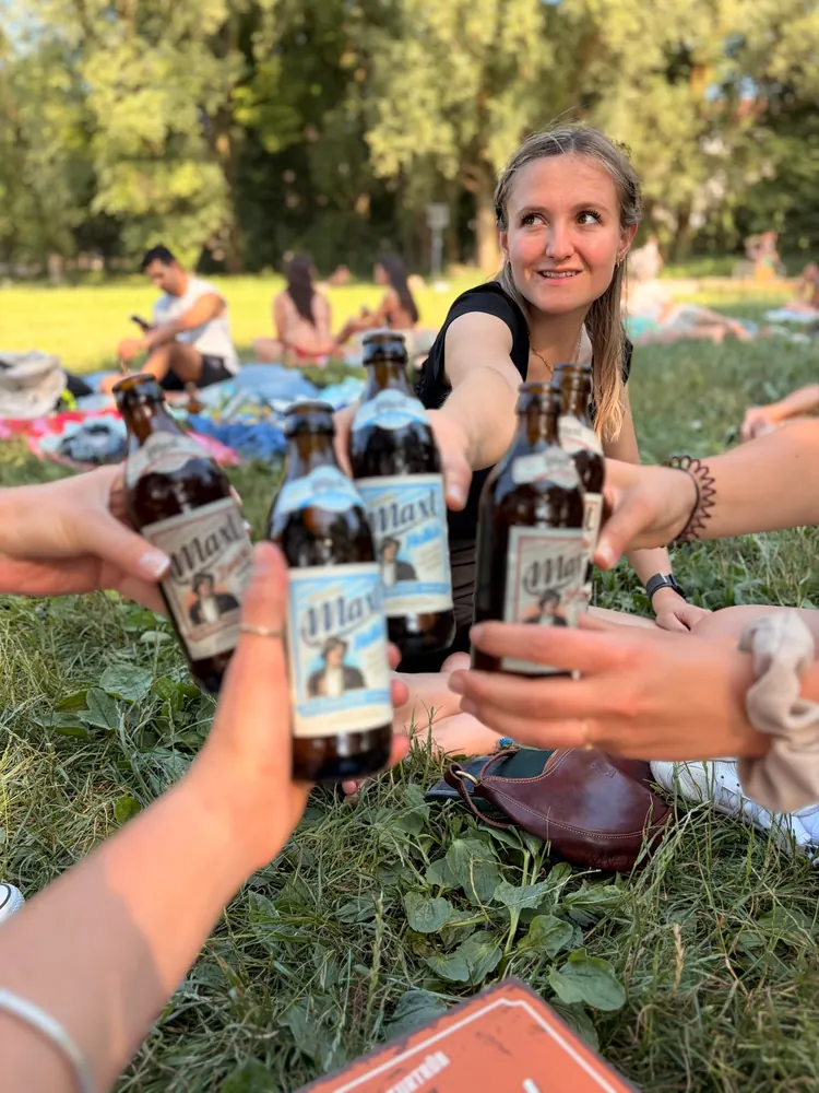 Vier Hände stoßen über einer Picknickdecke mit Maxl an