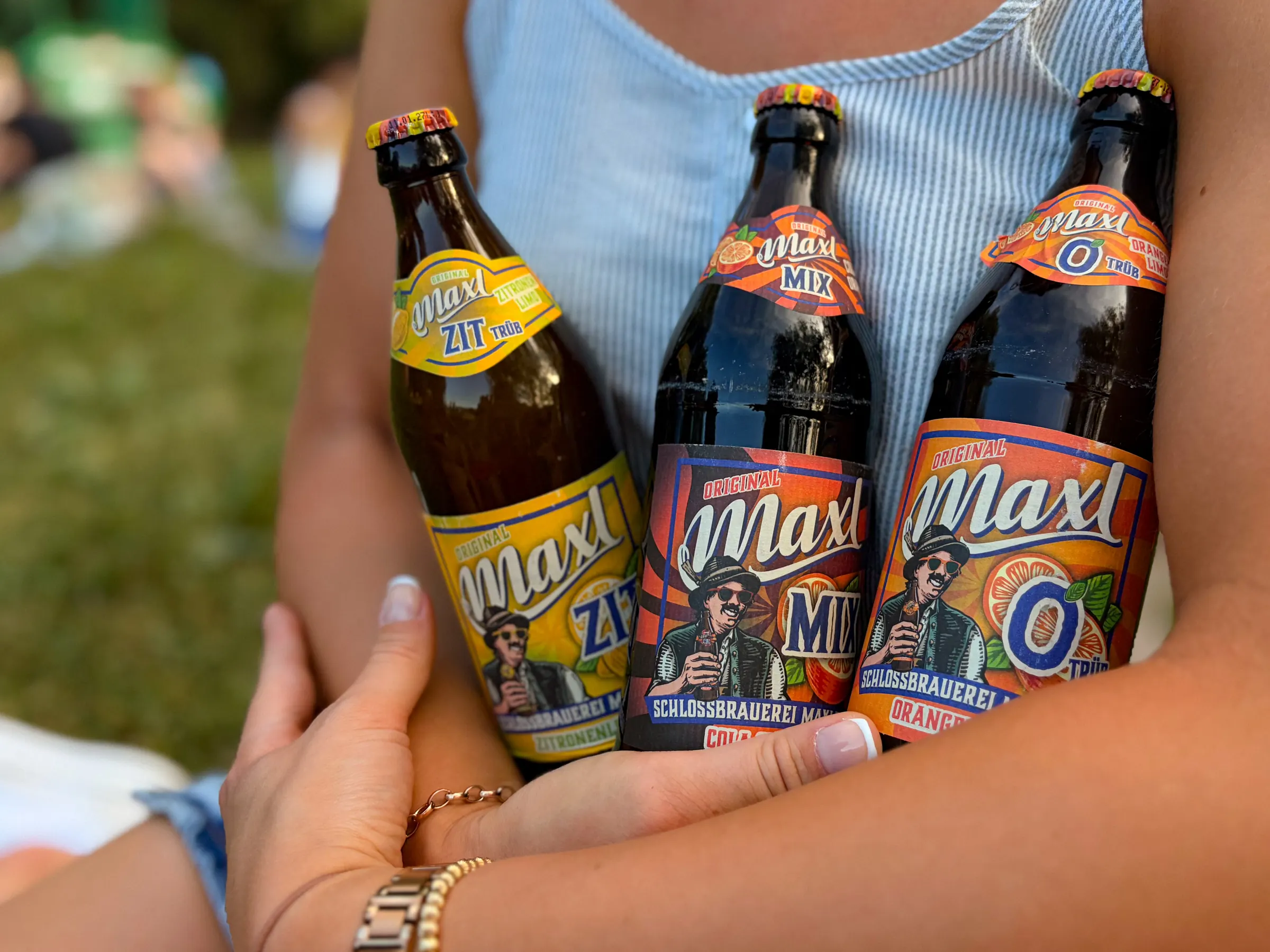 Drei Maxl-Limonaden – Zit, Mix und O – im Arm, auf einer Wiese im Sommer